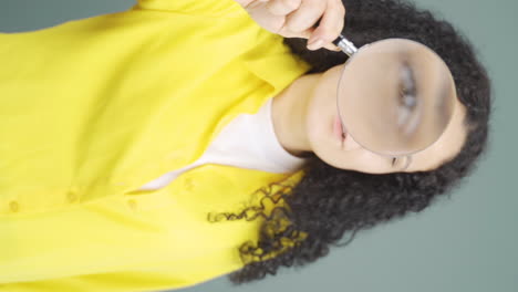 Vertical-video-of-Young-woman-looking-at-camera-with-magnifying-glass.