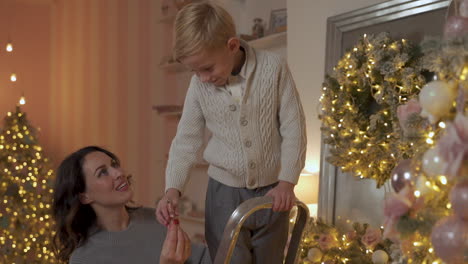 niño decora el árbol de navidad con estrellas y adornos, su madre lo ayuda