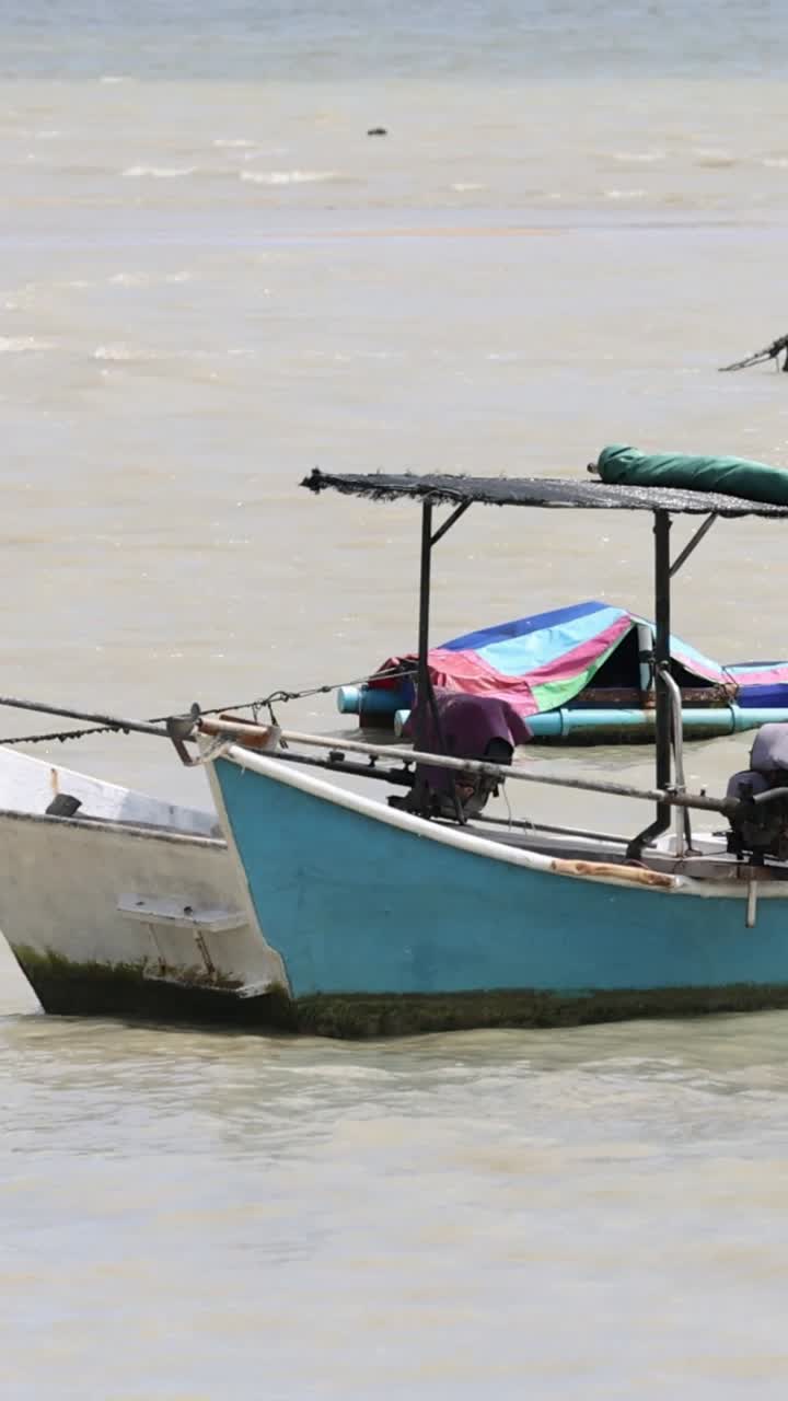 A traditional longtail boat gently rocks in the waters off Phuket, Thailand, showcasing local fishing culture under bright daylight