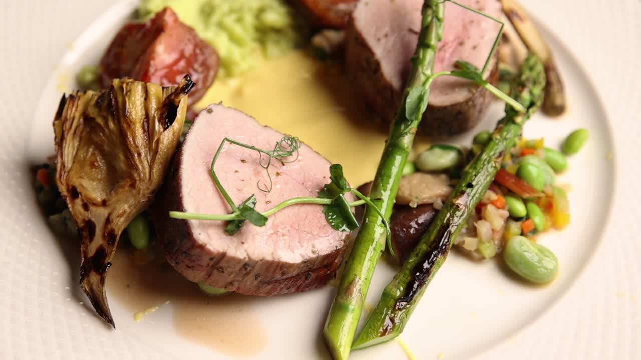 Filetto di Maiale Gourmet con Asparagi e Carciofi Arrostiti su un Piatto Bianco