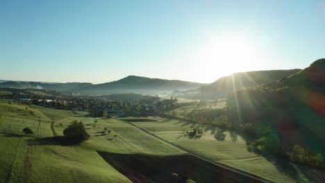 relaxing aerial shot of countryside village in switzerland during morning sun, beautiful sunny day with very green agricultural fields