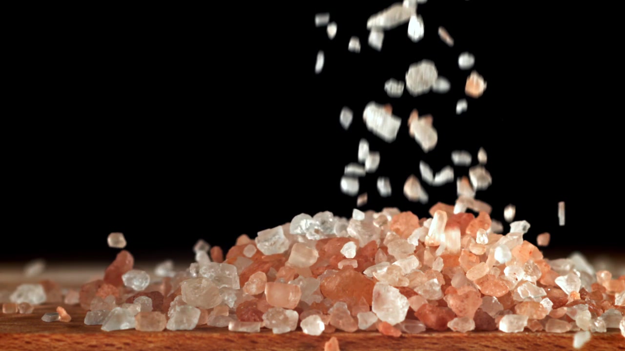 Movimento rallentato di sale rosa dell'Himalaya che cade su sfondo nero
