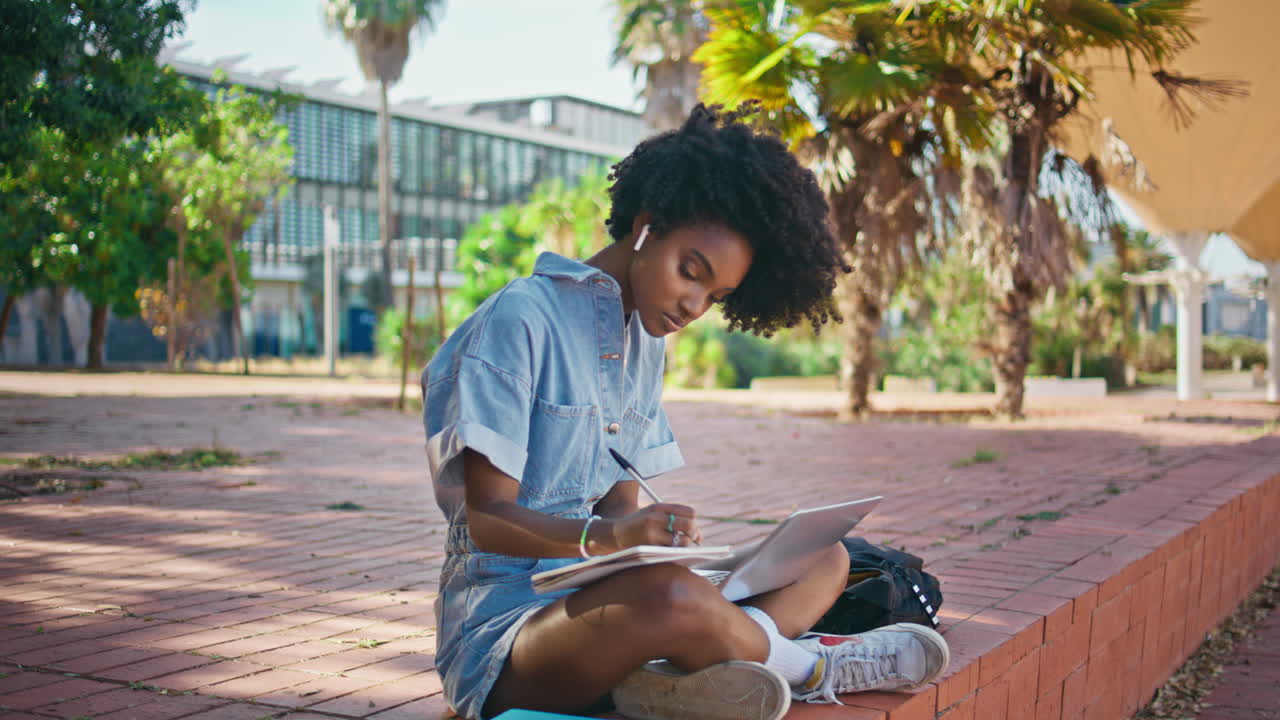 Girl writing notebook doing college homework on street. Student studying