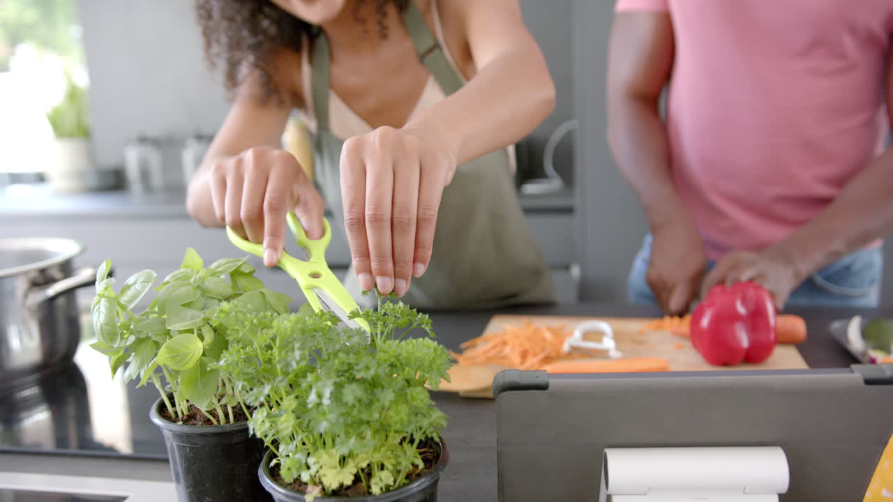 Cutting fresh herbs with scissors, woman cooking with man chopping vegetables