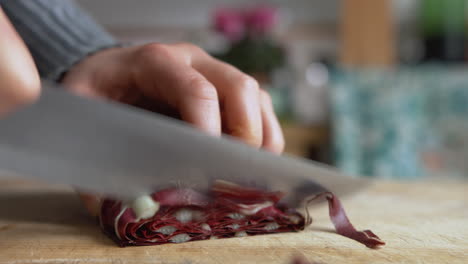 Close-up-woman's-hand-start-slicing-Italian-chicory-with-a-sharp-knife-on-a-wooden-board-in-her-kitchen