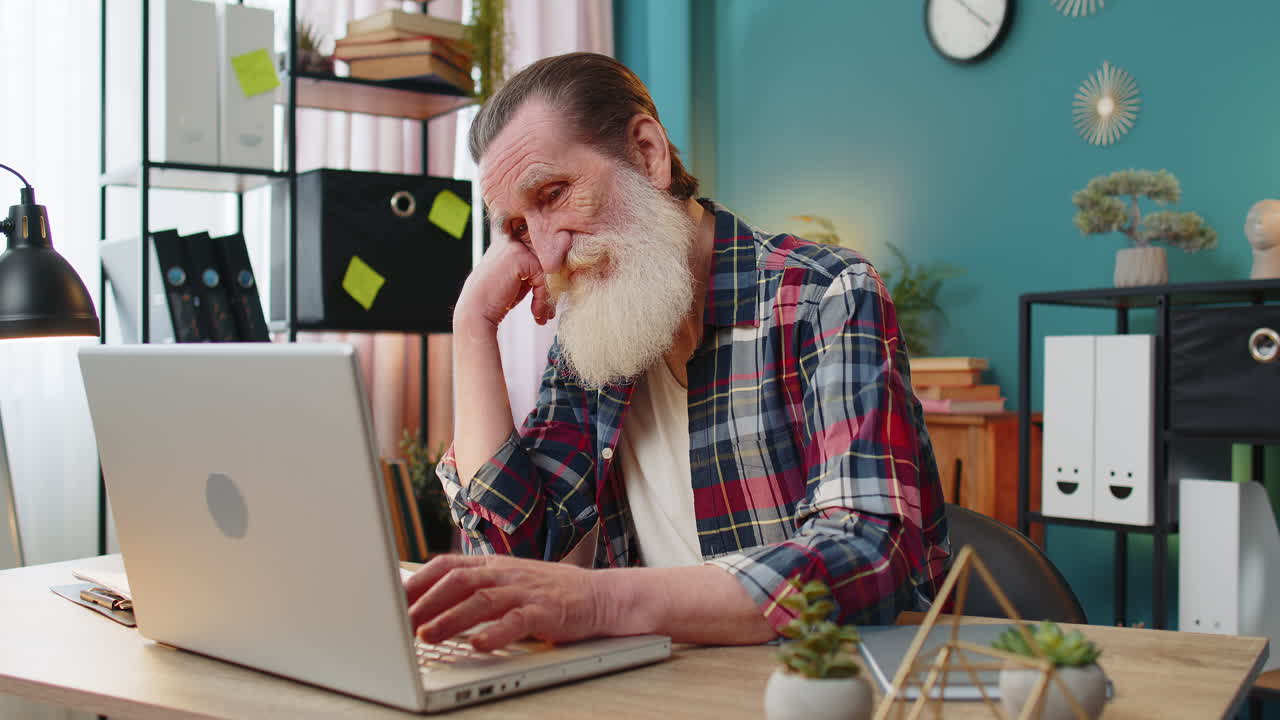 Overtired sleepy lazy senior man grandfather bored working on laptop while sitting in home office