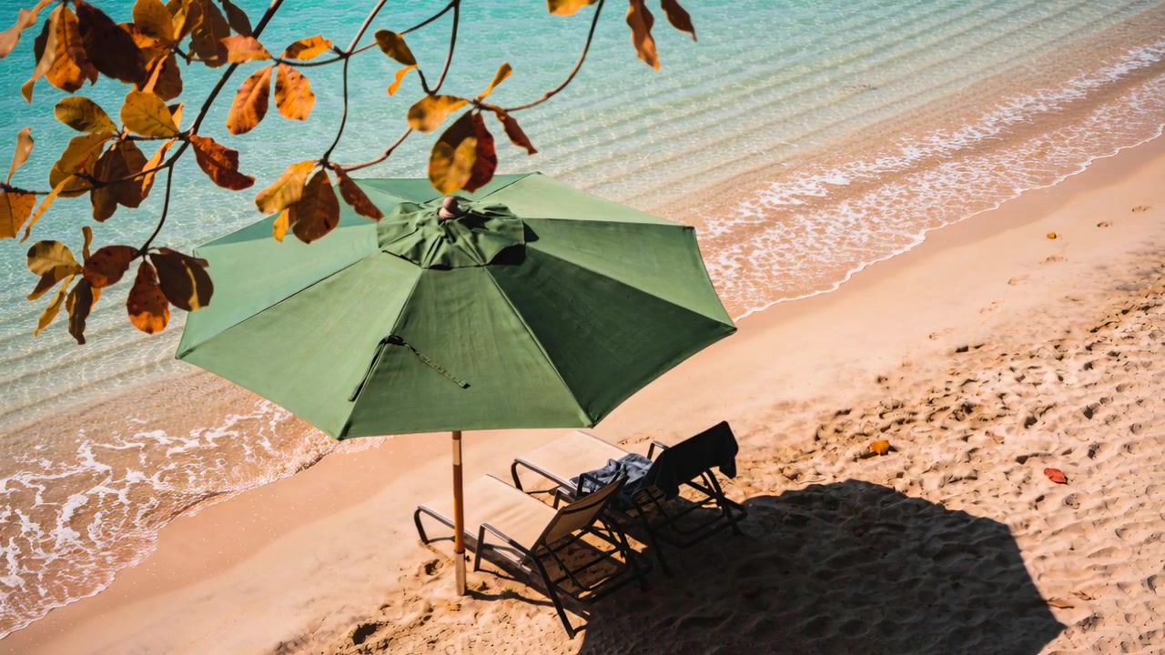 La caméra descend en panoramique, dévoilant du sable ensoleillé et de l'ombre, un parasol ombrageant des chaises longues, une serviette et un sac.