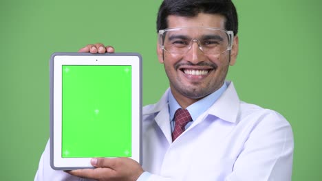 joven hombre persa apuesto médico con gafas de protección mostrando tableta digital
