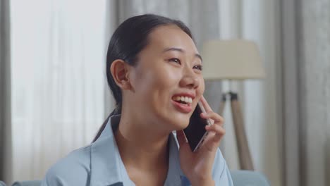 close up of asian woman talking on smartphone while sitting on sofa in the living room