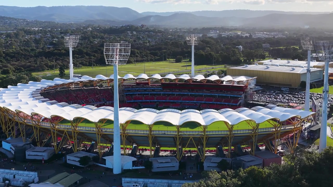 Wide aerial drone shot of a circular sports arena under bright daylight and clear skies.