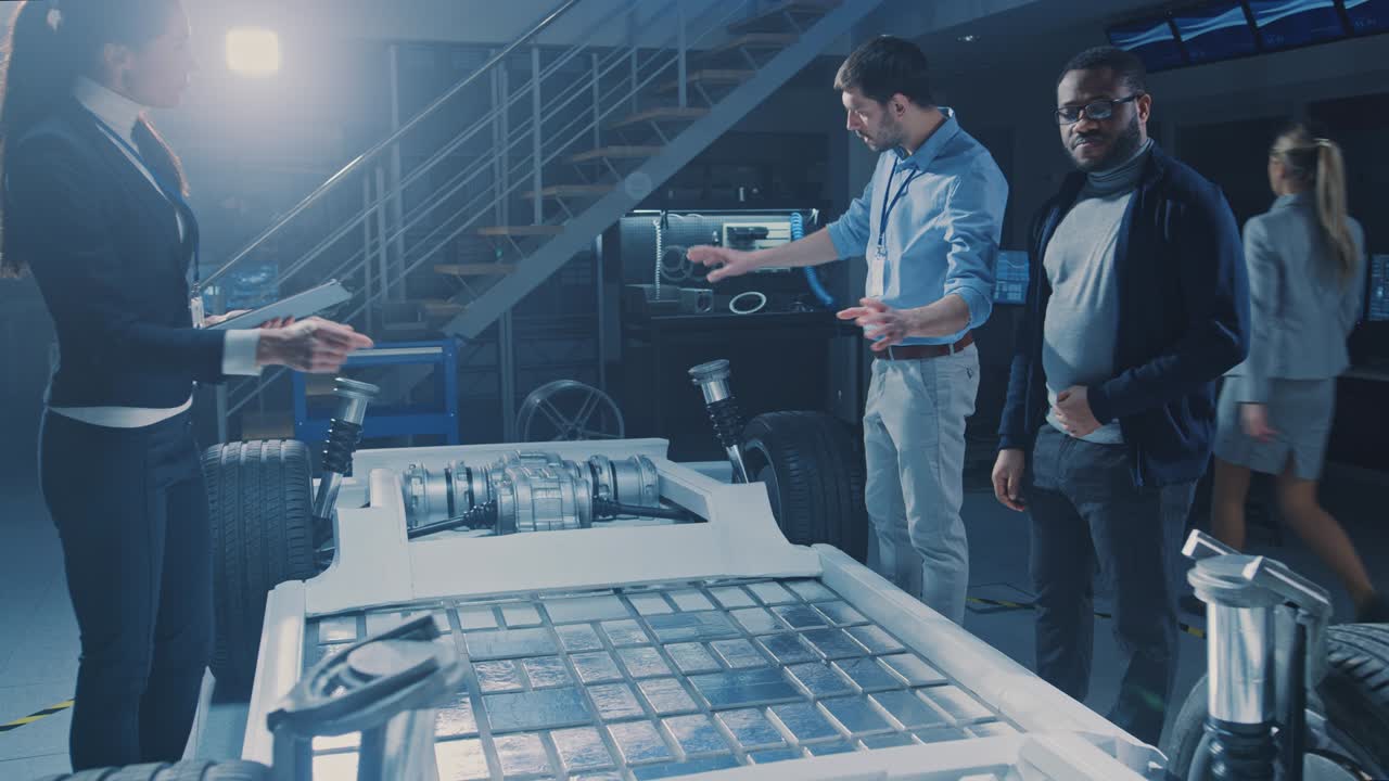 un team internazionale di ingegneri di progettazione automobilistica discute la progettazione di un prototipo di auto elettrica autonoma. il telaio della piattaforma del veicolo ha ruote, motori, batterie. evoluzione dell'efficienza dell'energia rinnovabile pulita