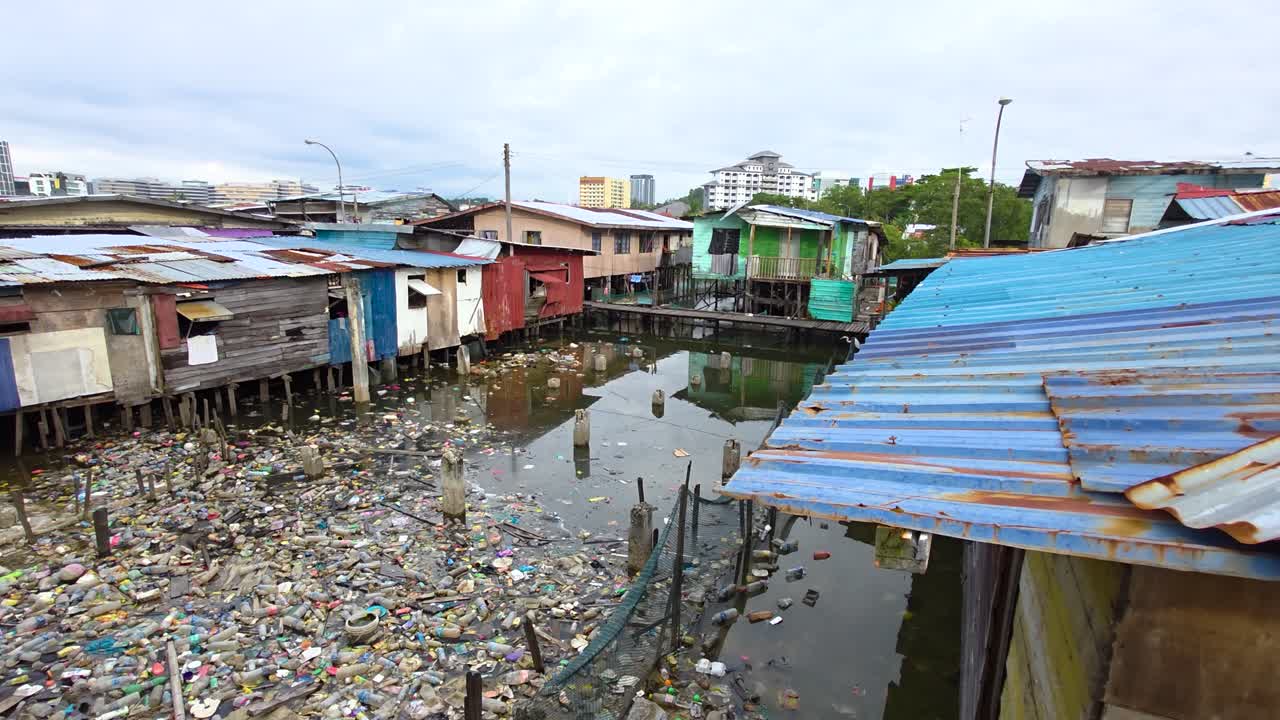 A reveal shot of a heavily polluted river filled with plastic garbage from stilt village locals living above water in Kota Kinabalu, highlighting urban environmental challenges