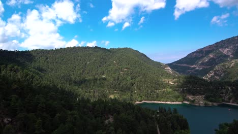 Toma-Aérea-Acercándose-Al-Lago-Tsivlou-En-Las-Montañas-Del-Peloponeso-De-Grecia-Con-Un-Cielo-Nublado-Brillante-Y-Nubes-Que-Proyectan-Una-Sombra-Oscura-Sobre-Los-Pinos