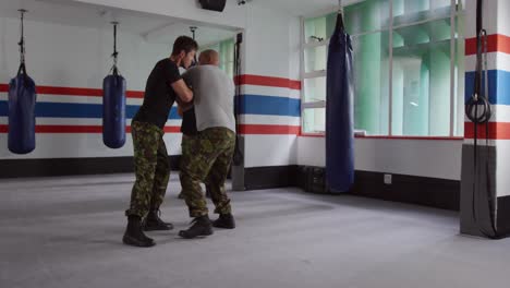 dos hombres caucásicos aprendiendo autodefensa de un entrenador en el gimnasio