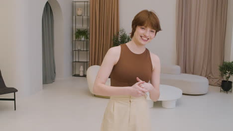 Girl-Wearing-Elegant-Clothes-Standing-In-The-Middle-Of-The-Living-Room-In-A-Modern-House-Smiling-And-Looking-At-The-Camera