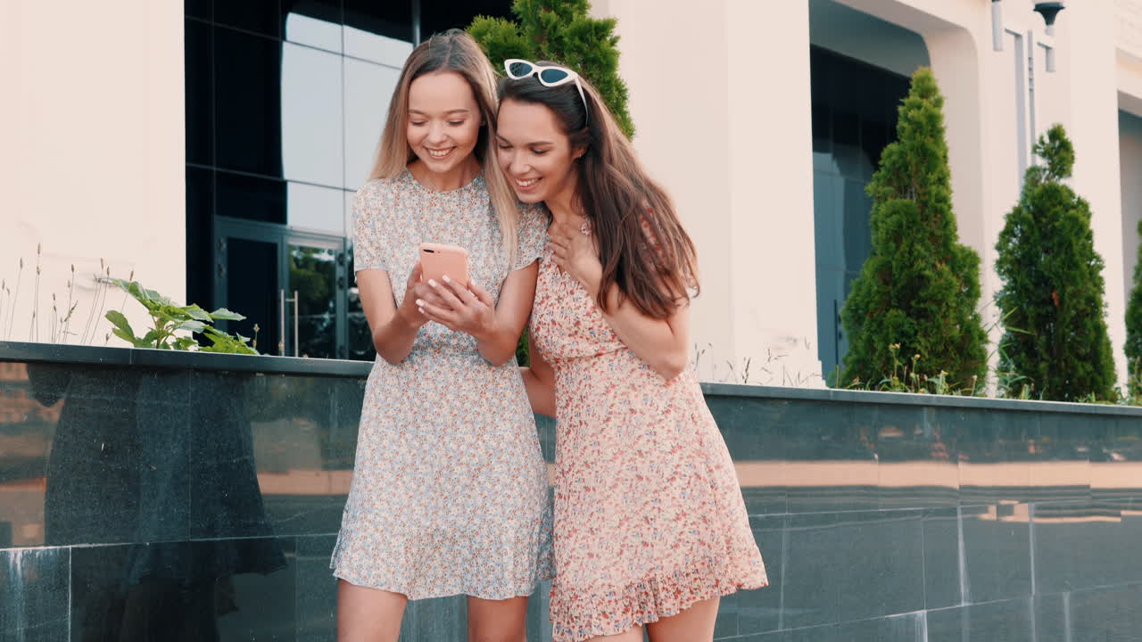 두 명의 행복한 여성들이 스마트폰을 보고 있습니다.