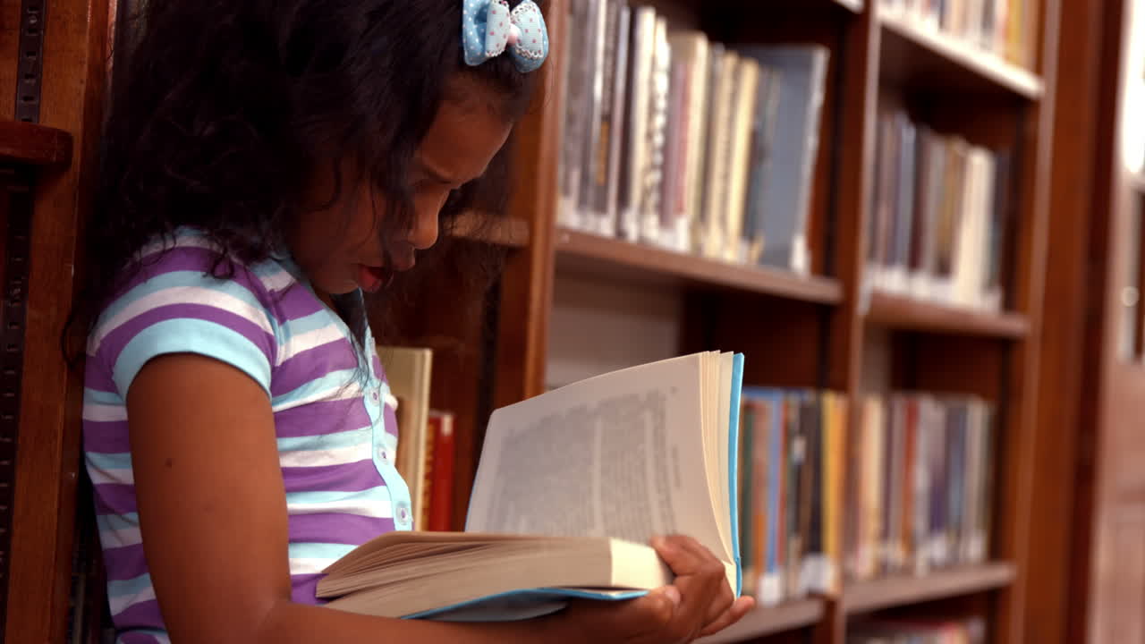 Cute pupil reading on library floor