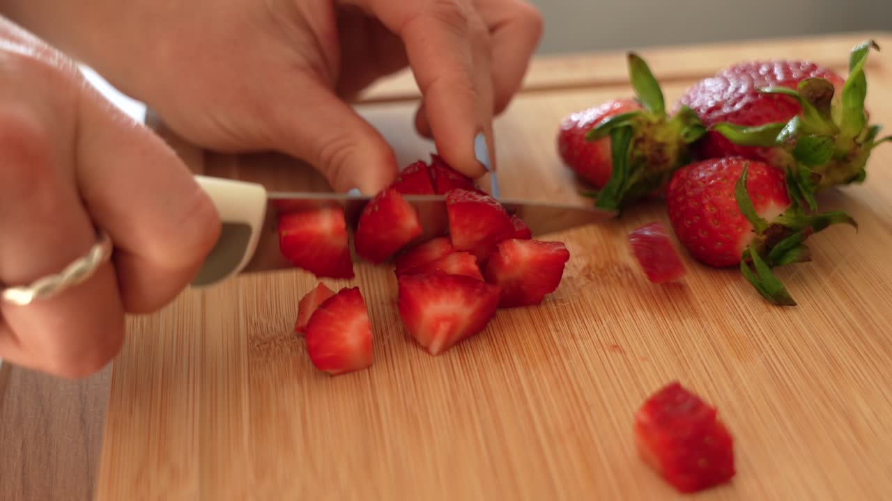 Female hands chopping strawberries with knife on wooden board