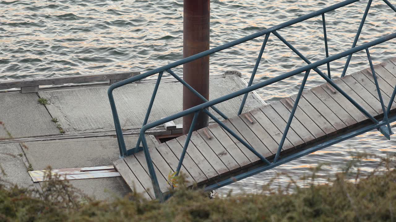 небольшая деревянная платформа с трапом на набережной, плывущая по блестящей речной ряби