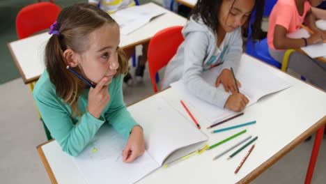 vista de alto ángulo de escolares de raza mixta dibujando en un cuaderno en el aula 4k