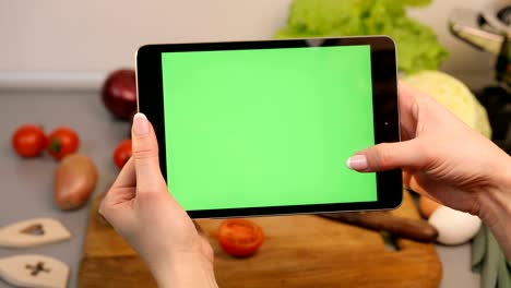 la mujer dispara su tableta en la cocina. las verduras están en el fondo.