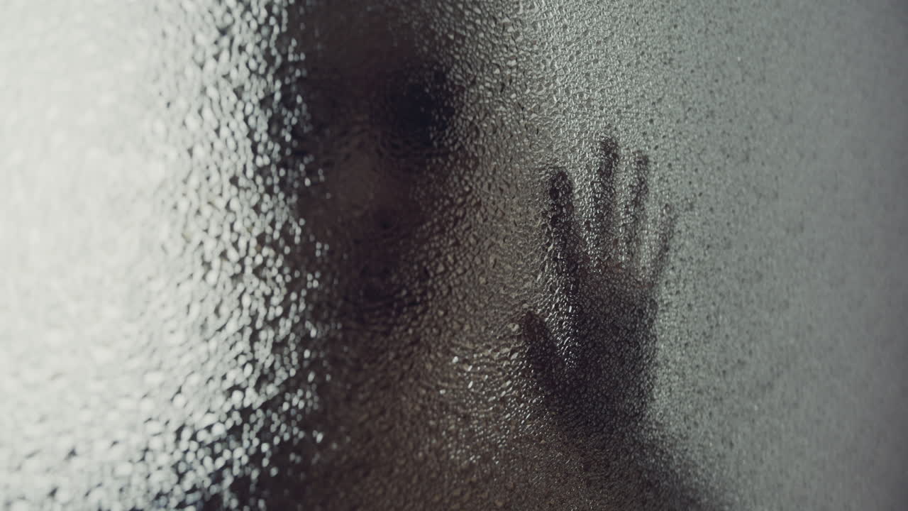 A female silhouette behind the frosted window touches the glass slowly
