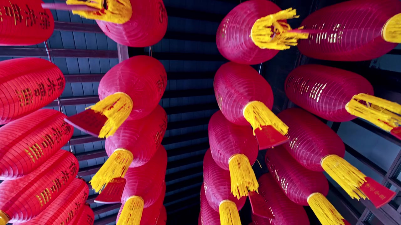 Lanternas vermelhas brilhantes com borlas amarelas estão suspensas do teto, criando uma exibição vibrante em um templo de Xangai. Ideal para documentários culturais ou reportagens de viagem.