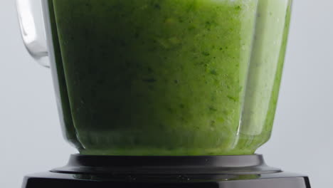 green smoothie blend mixing inside blender bowl in super slow motion close up.