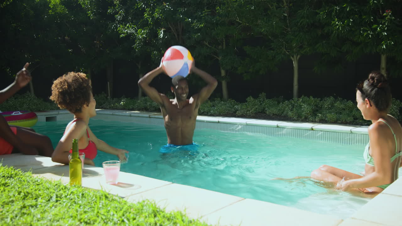 Vielfältige Freunde genießen die Zeit am Pool, spielen mit einem Wasserball, entspannen und lachen zusammen.