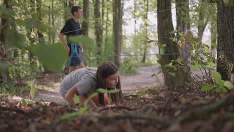 children in a summer camp hike crawls on the ground. training of passing obstacles by crawling on the ground. a girl tumbles in the forest on a camp assignment