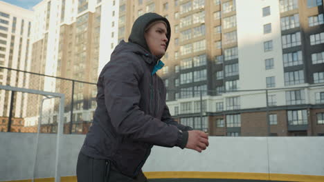 focused athlete in profile view clasping hands during outdoor workout session on urban sports ground surrounded by high-rise residential buildings and goal post under soft daylight