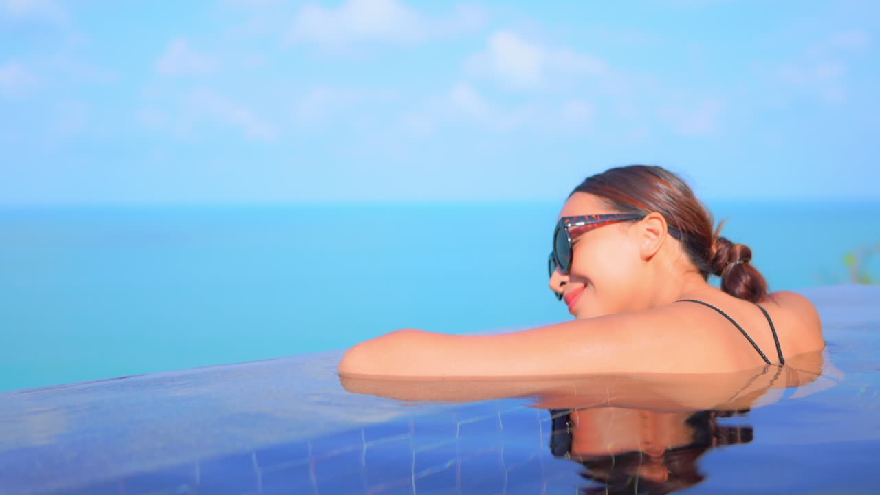 Woman in Sunglasses Relaxing Leaning her Head on the Hands in the Border of Infinity Pool, daytime Miami