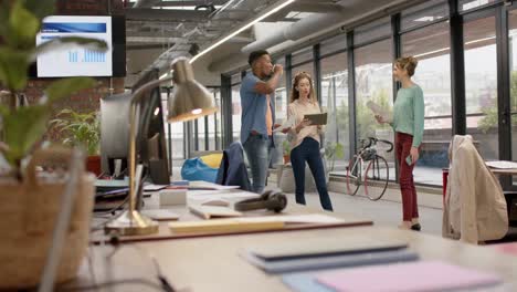 diverse casual business colleagues with tablet and paperwork standing in office talking, slow motion