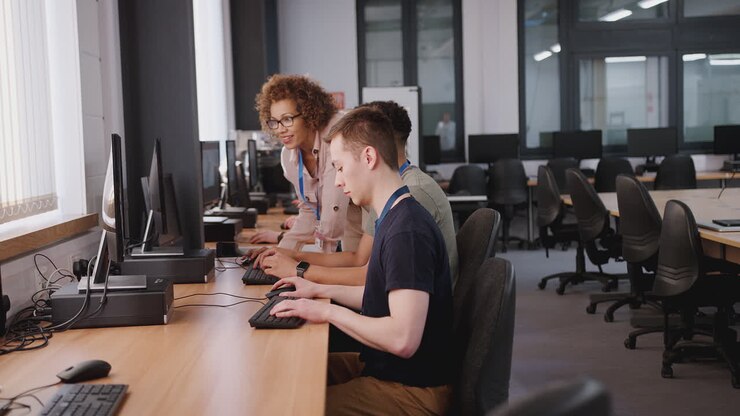 Group Of College Students With Tutor Studying Computer Design Sitting At Monitors In Classroom