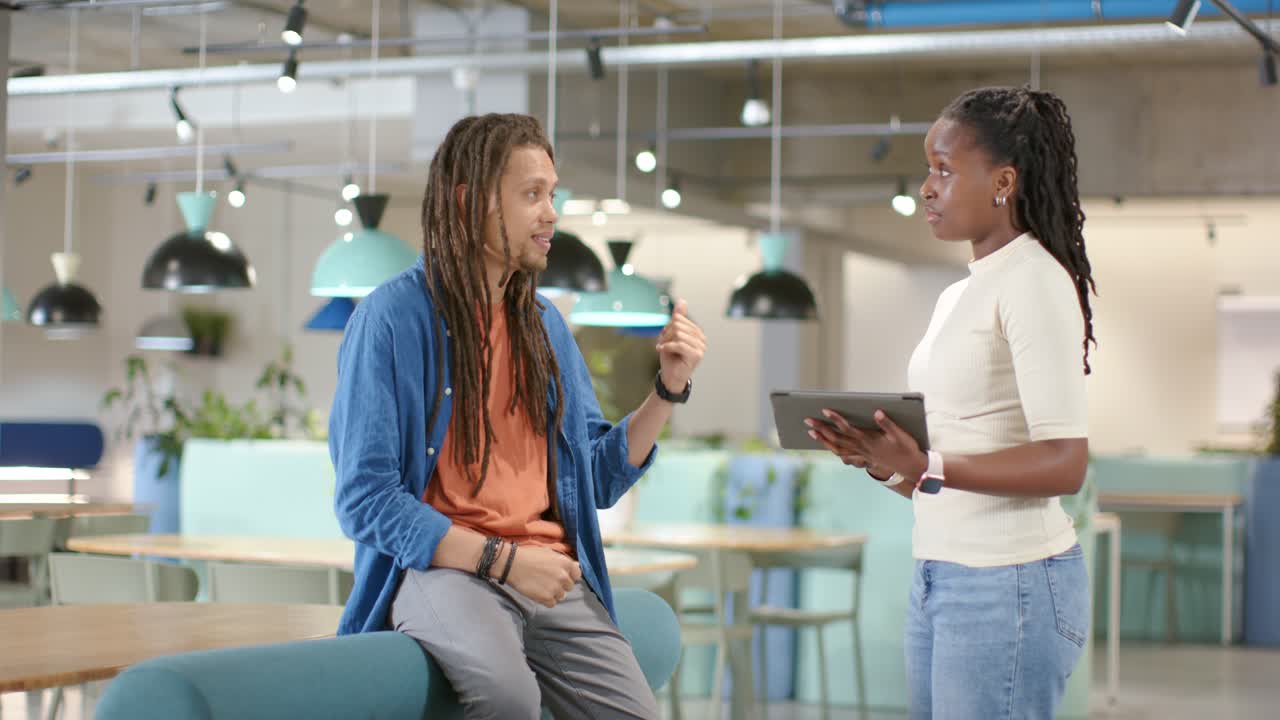 African American coworkers woman holding tablet checking notes, man gesturing and explaining idea