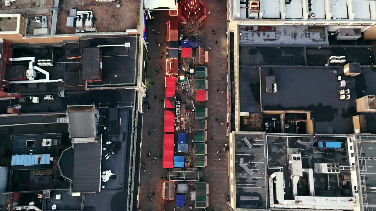 Bird’s-eye aerial drone shot of Southampton’s Christmas Market in winter at sunset, showing rows of festive stalls, glowing lights, and crowds moving through the square under the soft evening sky