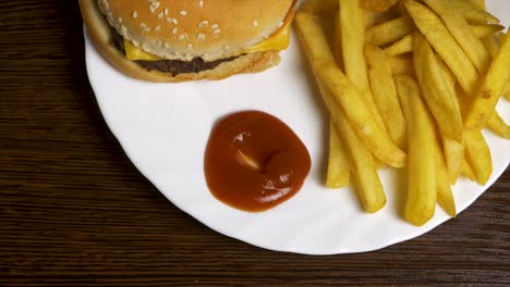 hand dipping french fries in ketchup with a cheeseburger on a plate