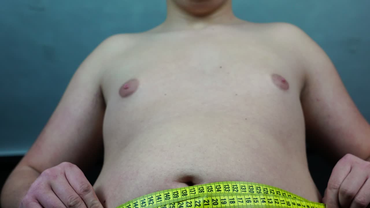 미터 테이프로 배 둘레를 측정하는 남자, 낮은 각도를 닫습니다.