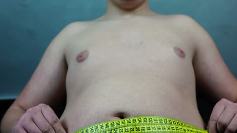 man measuring his belly circumference with meter tape, close up low angle