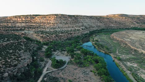 Aerial pull out shot of the landscape of the San Juan river at sunset. Featuring cliffs and a blue river.