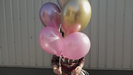 mujer bonita en vestido sosteniendo globos con helio al aire libre a la luz del día