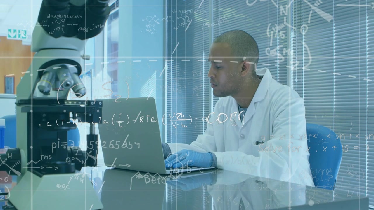 Male lab technician opening laptop and typing, bringing overlays onto microscope view for research