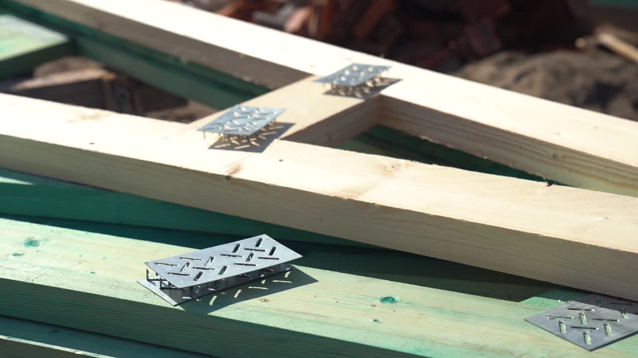 Metal nail plates and timber beams arranged on ground at sunny construction site