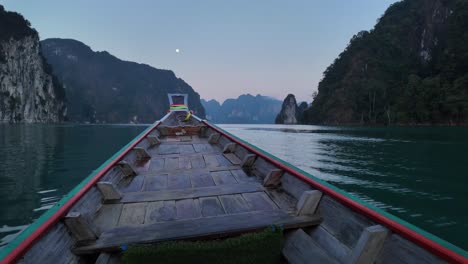 A-vessel-smoothly-traversing-the-waters-of-Khao-Sok-National-Park-in-Surat-Thani,-Thailand,-as-dusk-sets-in,-accompanied-by-the-moon-on-the-horizon,-encapsulating-the-essence-of-travel-and-leisure