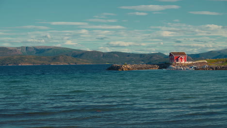 red wooden house in a fjord, norway. scenic cinemagraph of blue ocean with harbor pier and boats and ships.