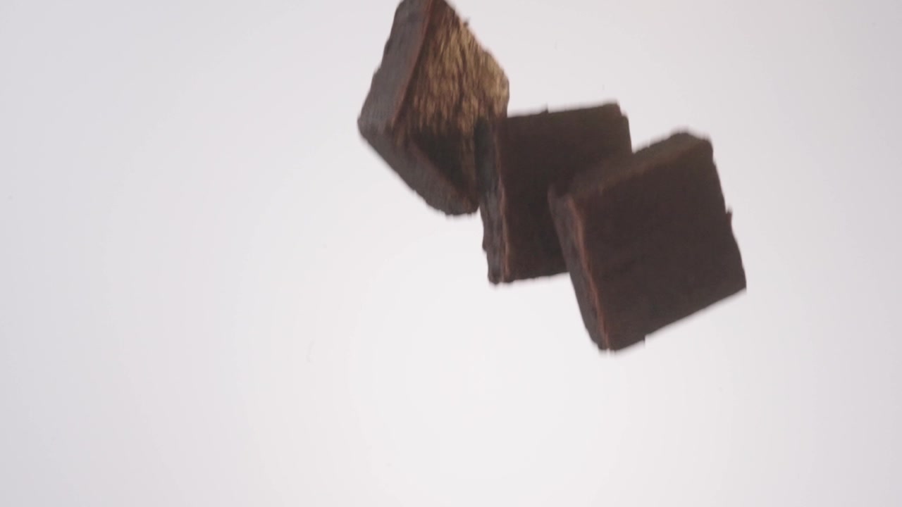 Rich fudgy brownies raining down on white seamless backdrop in cinematic slow motion. bake sale fundraisers, school lunch content, party dessert tables.