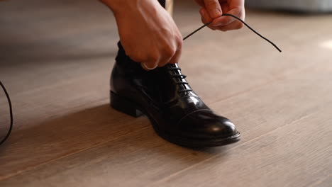 the groom puts on black shoes and ties his shoelaces - close up