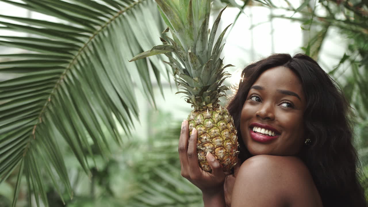 Shooting in profile young beautiful girl holding a pineapple and smiling at the camera against the