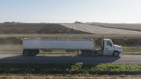 aerial, semi truck with hopper trailer driving on rural countryside farm road during daytime