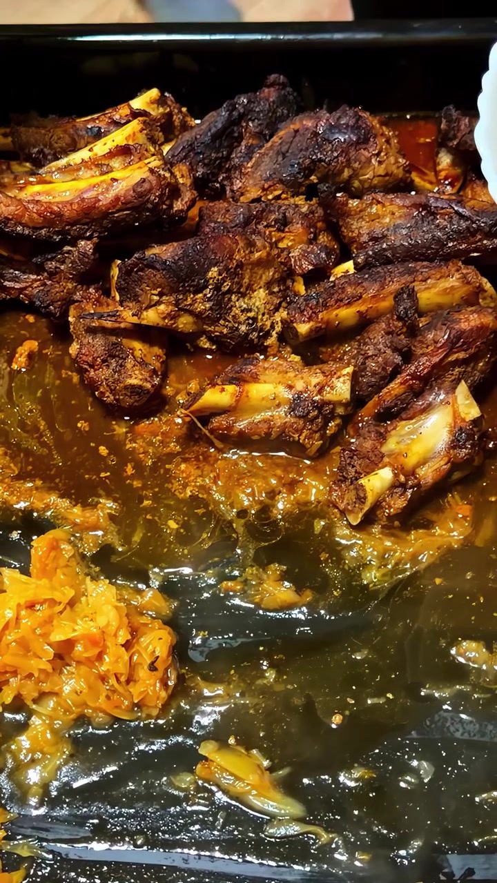 Costine di manzo cotte e condite con spezie, servite da un vassoio insieme a una ciotola di verdure sottaceto, che evidenziano texture ricche e colori vivaci